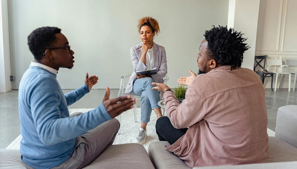 two men have an argument while a woman in a chair listens
