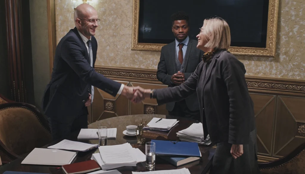 2 people professionally dressed shaking hand while a third individual observes