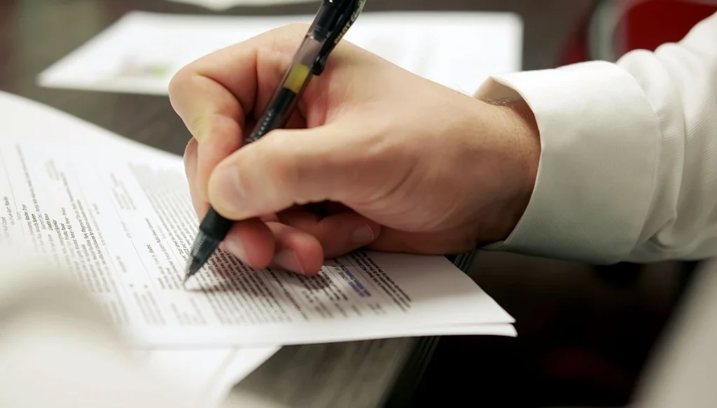 hand holding a pen over some documents