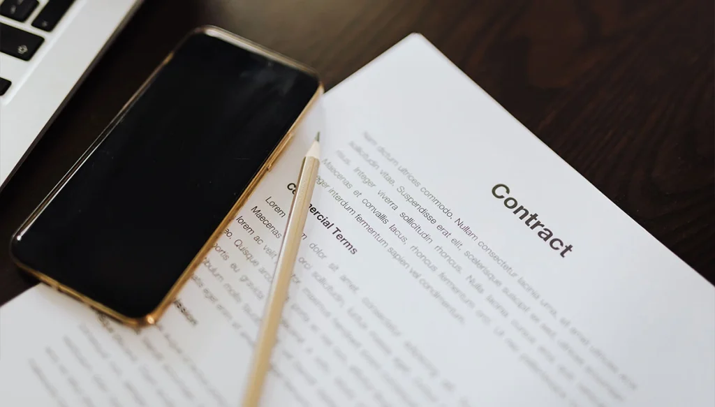 a contract with a cellphone and a pencil on a desk.