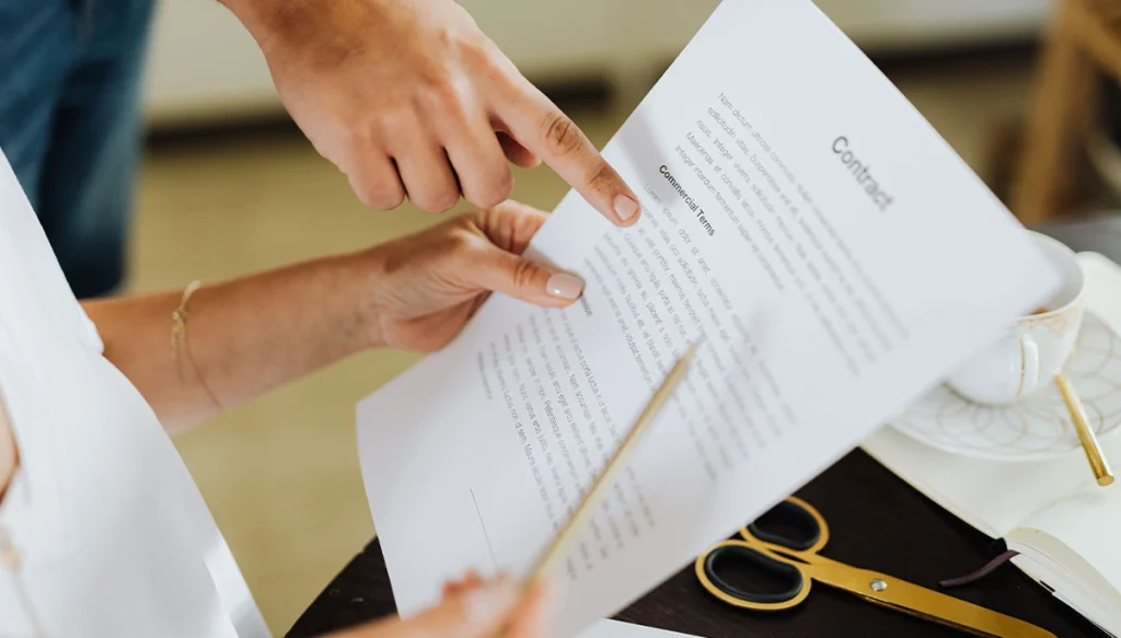 hands of persons holding an pointing at the details of a contract.